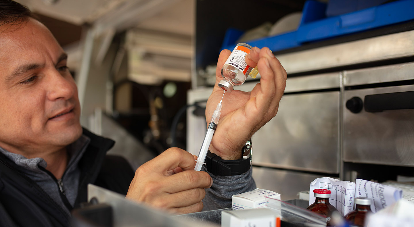 Person preparing a syringe with a bottle of medication.