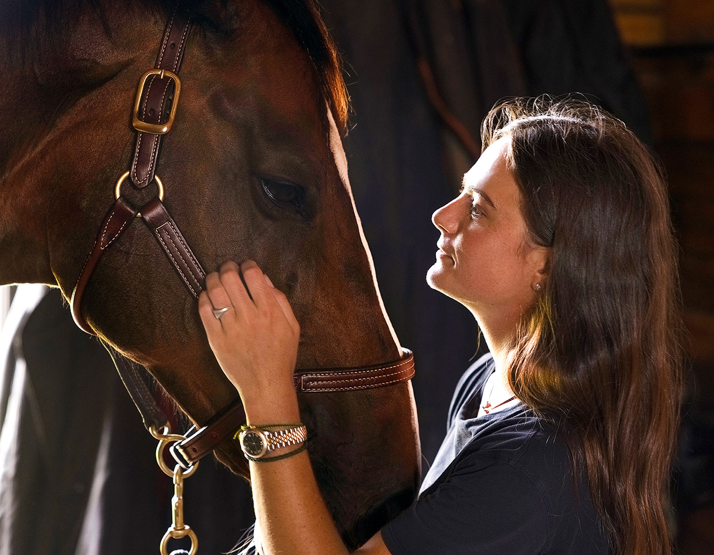 Woman gently holding a horse's face in a stable, close-up portrait